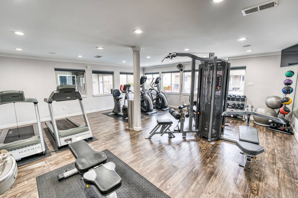 a gym with cardio equipment and weights on a wooden floor at Juniper Springs Apartments, Austin, TX